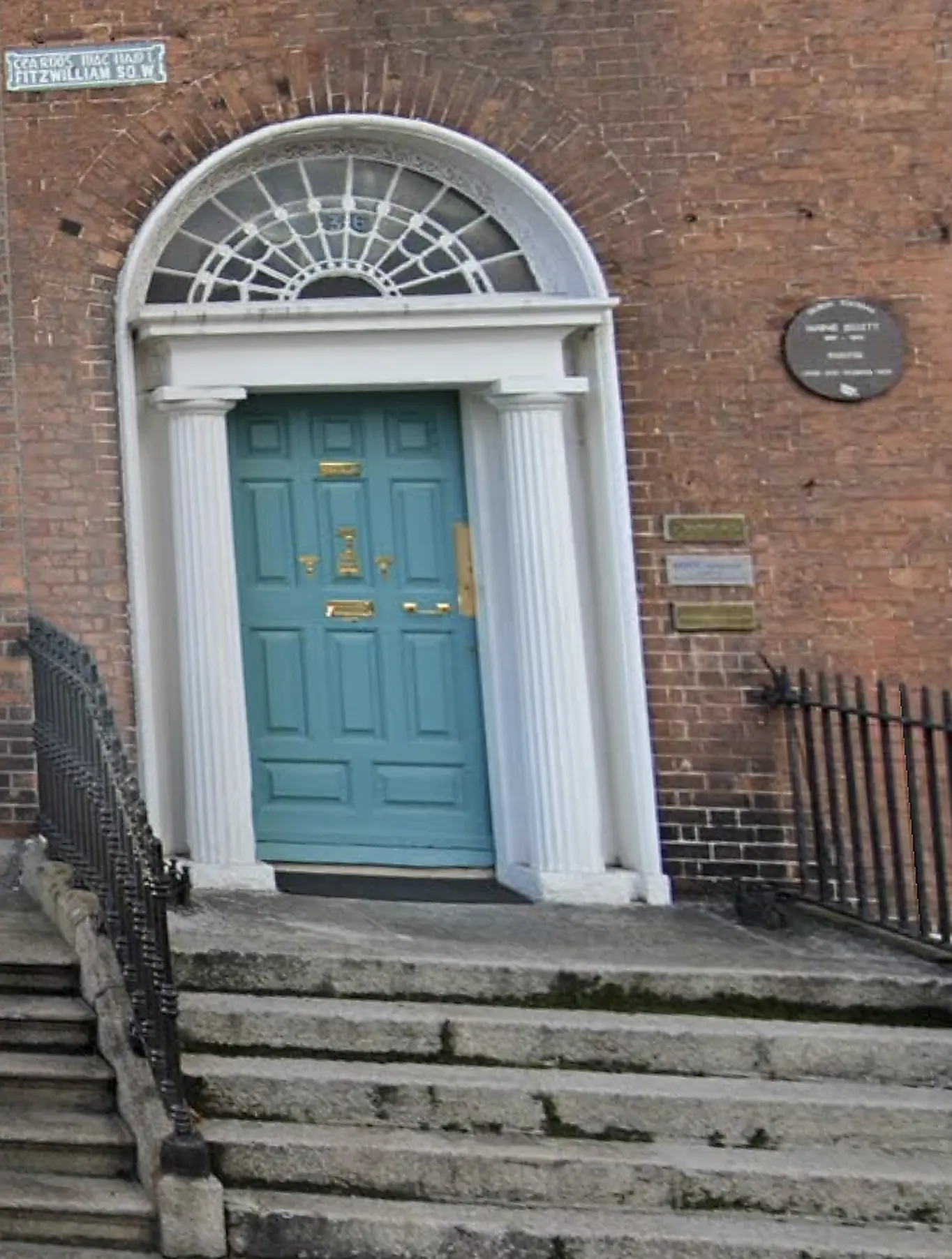 Blue-green Georgian doorway with a semicircular fanlight, white columns, granite steps and black railings at 36 Fitzwilliam Square West, Dublin.